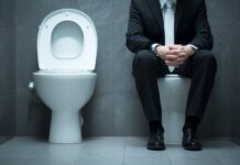 7 Early Warning Signs That Call for a Urologist Visit Man in a business suit sitting on a toilet, symbolizing possible urological health issues and the importance of recognizing early warning signs.