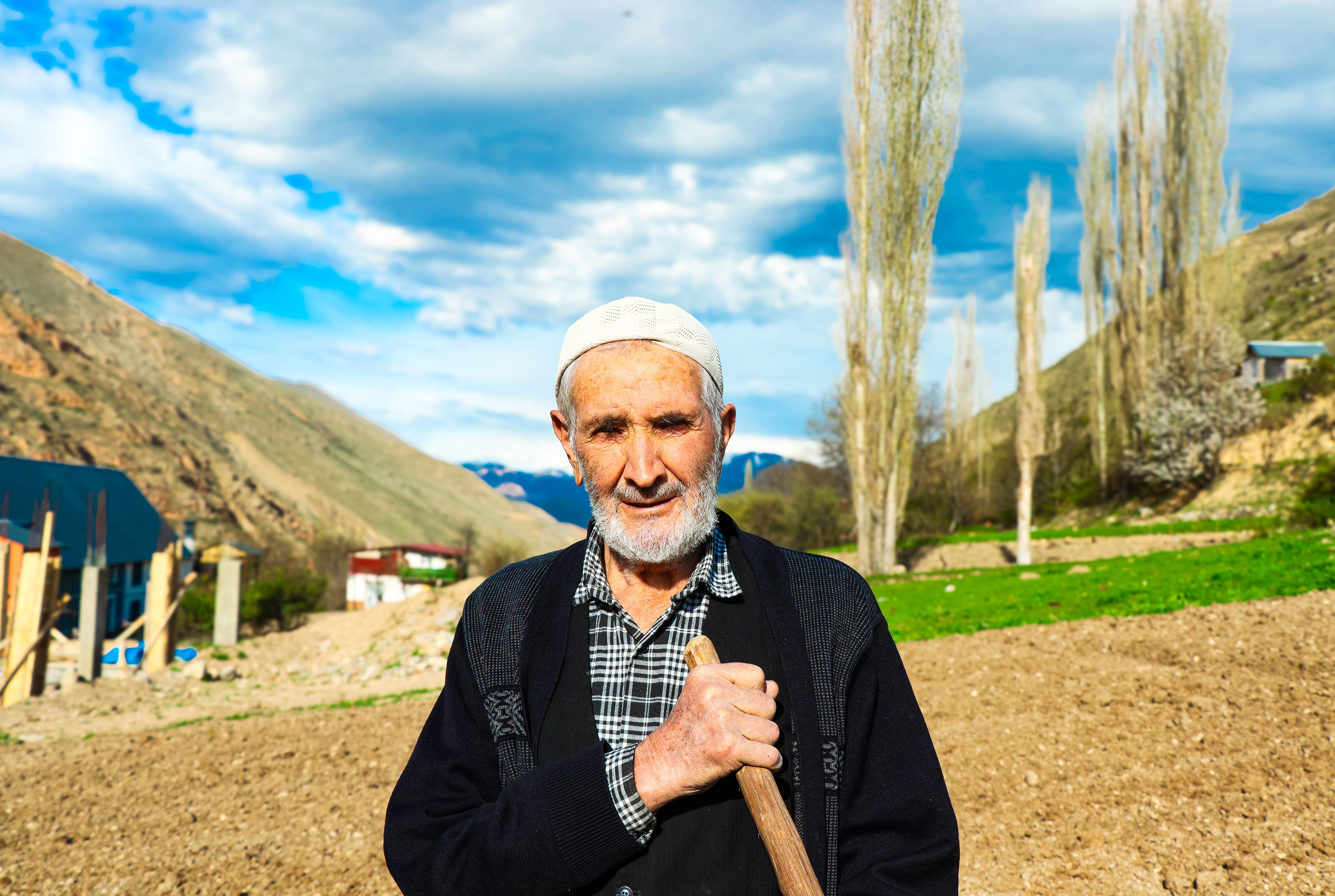 Elderly rural farmer holding a hoe in front of hills and fields