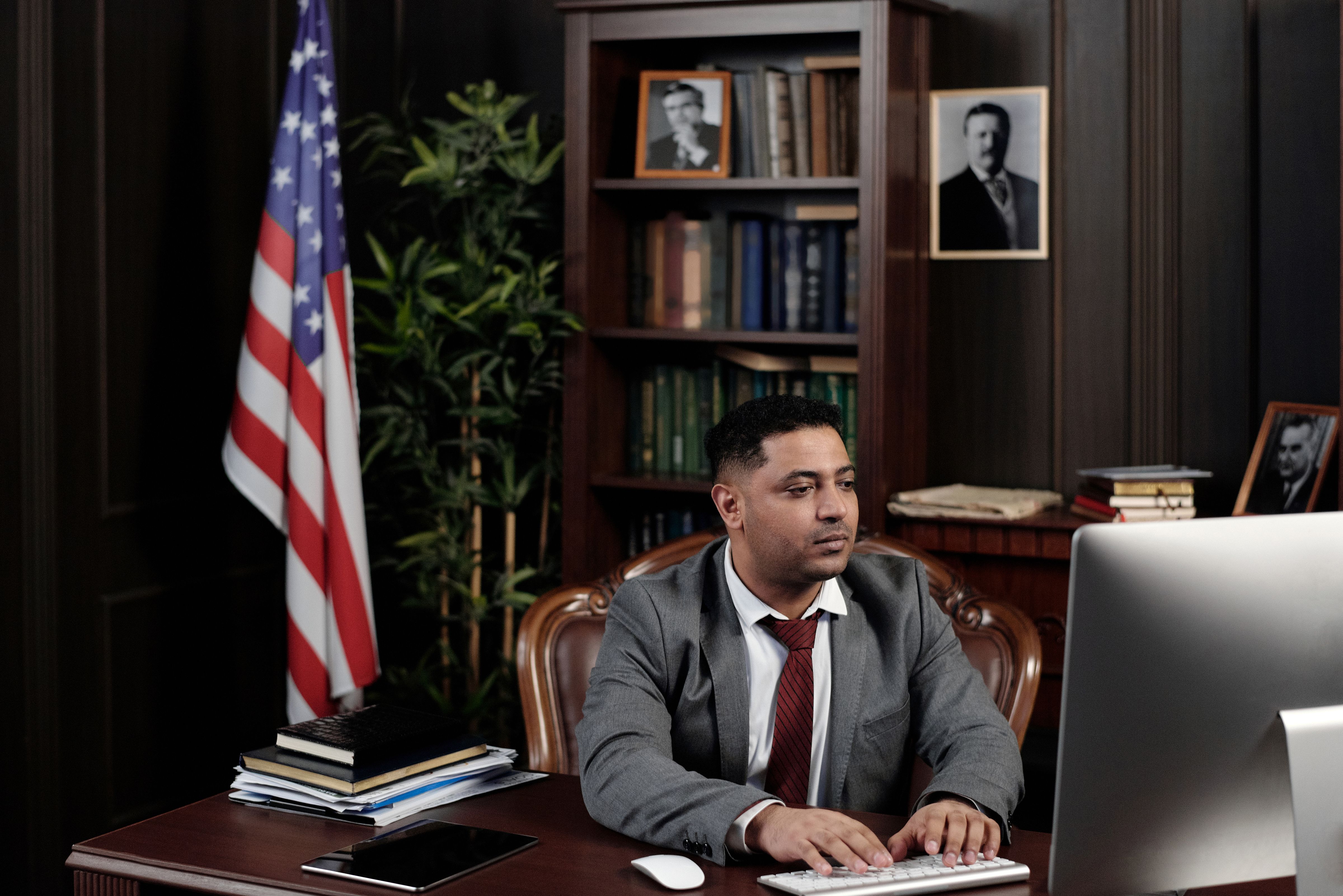 Senior male public official in a suit working at his desk with an American flag behind him