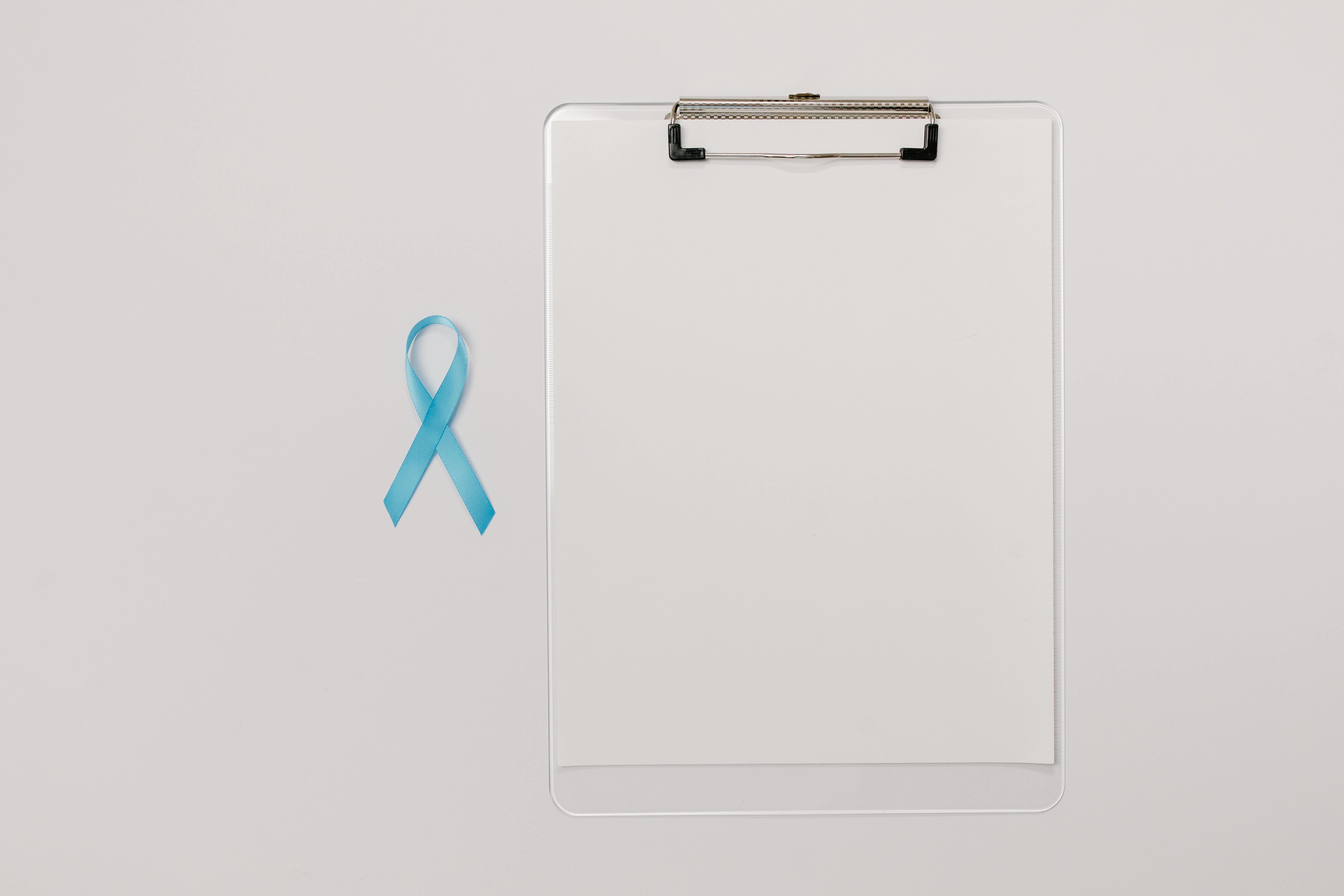 Flat lay of a blue prostate cancer awareness ribbon beside a medical clipboard