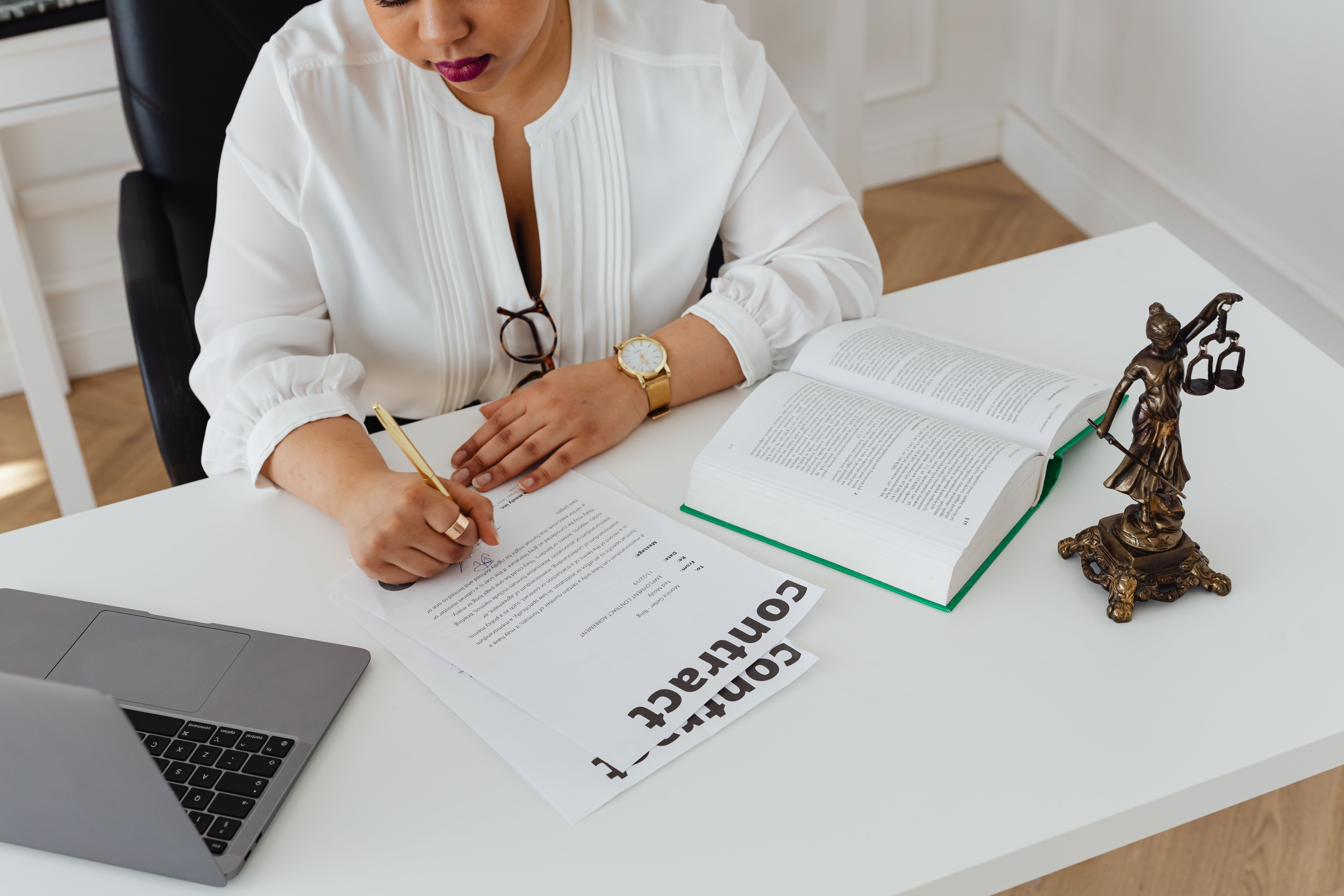 Woman reviewing contracts and legal papers at a desk with law books and laptop